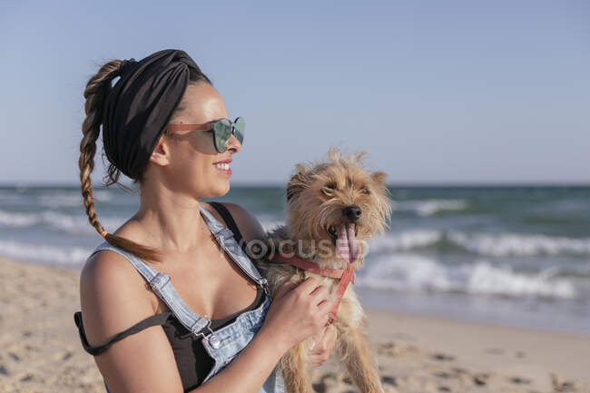 Mujer sosteniendo su perro en la playa - foto de stock