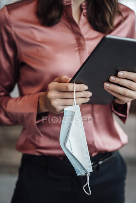 Female entrepreneur holding digital tablet and protective face mask at cafe — Stock Photo
