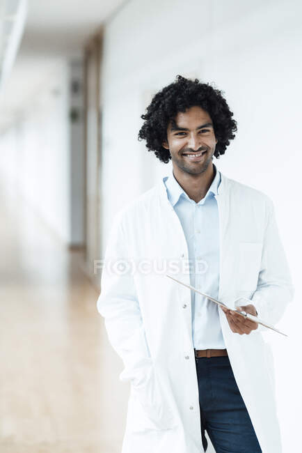 Усміхнений молодий працівник охорони здоров'я тримає кишеню, стоячи в лікарняному коридорі — стокове фото