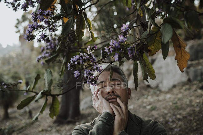 Älterer Mann berührt Gesicht, während er unter blühendem Baum im Garten steht — Stockfoto