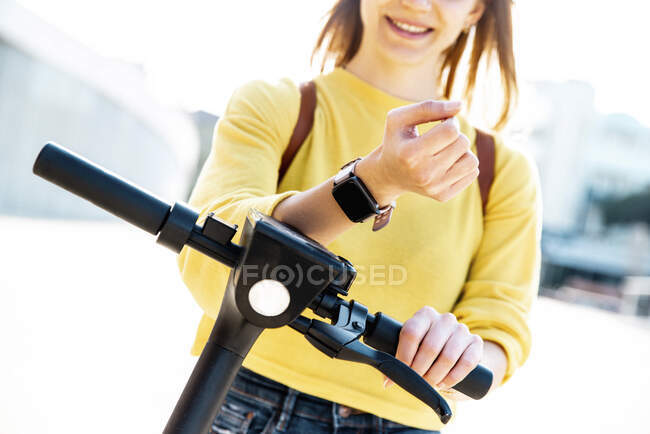 Woman with smart watch unlocking electric push scooter — Stock Photo