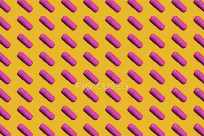 Pattern of rows of pink medicine capsules laid against yellow background — Stock Photo