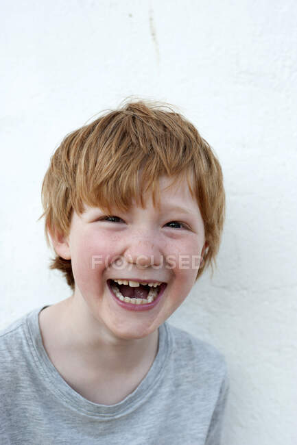 Сміється рудий хлопчик перед білою стіною — стокове фото