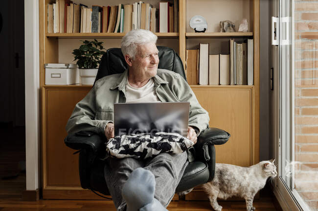 Smiling senior man with cat looking through window at home — indoors, shelf  - Stock Photo | #489912316