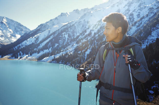 Mujer con mochila mirando hacia otro lado mientras sostiene bastones de senderismo por montaña - foto de stock