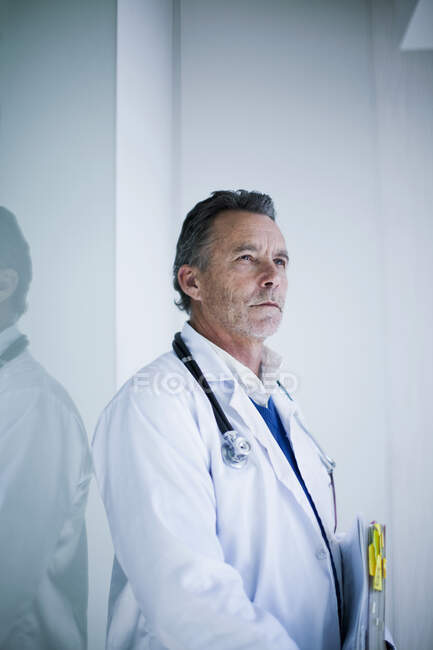 Médico senior masculino con documentos de pie en el hospital - foto de stock
