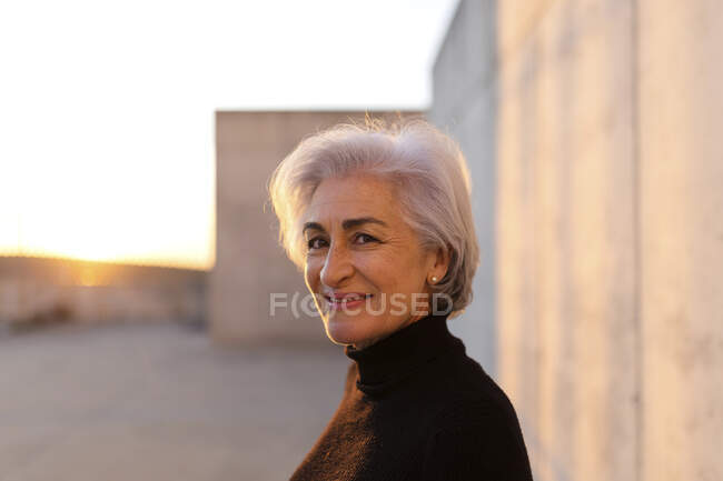 Mujer madura con el pelo gris sonriendo delante de la pared - foto de stock