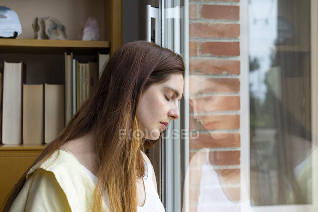 Sad woman with eyes closed leaning on window at home — Stock Photo