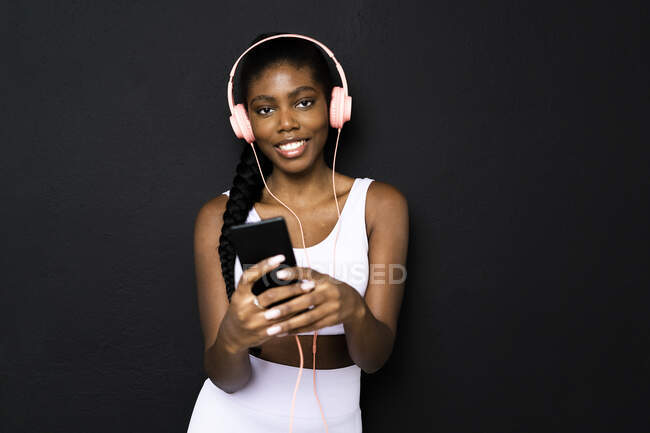 Junge Frau hört Musik über Kopfhörer vor schwarzem Hintergrund — Stockfoto