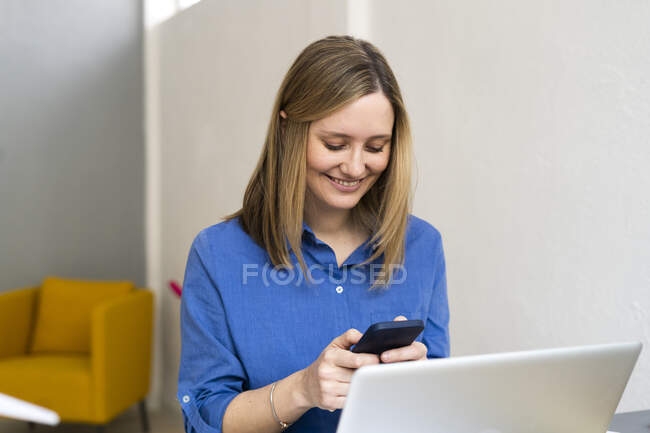 Empreendedora sorridente usando telefone celular enquanto trabalhava no escritório — Fotografia de Stock