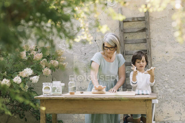 Petit-fils jouant avec la pâte tandis que grand-mère pétrissant la pâte à la cour arrière — Photo de stock