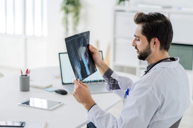 Trabalhador de saúde do sexo masculino analisando raio-X enquanto sentado na mesa no hospital — Fotografia de Stock