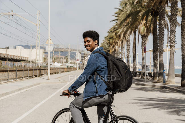 Sorrindo homem carregando mochila enquanto andar de bicicleta na estrada — Fotografia de Stock