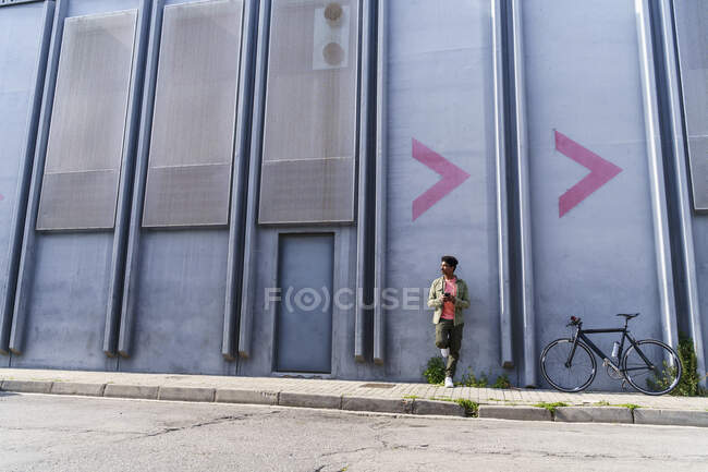 Mann schaut weg, während er sich an Fabrikwand lehnt — Stockfoto