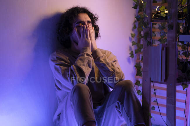 Triste hombre sentado con la cabeza en las manos en casa - foto de stock