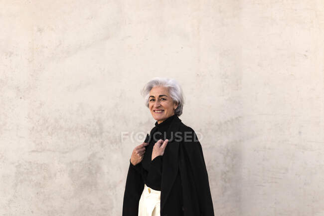 Lächelnde reife Frau trägt Jacke an Wand — Stockfoto