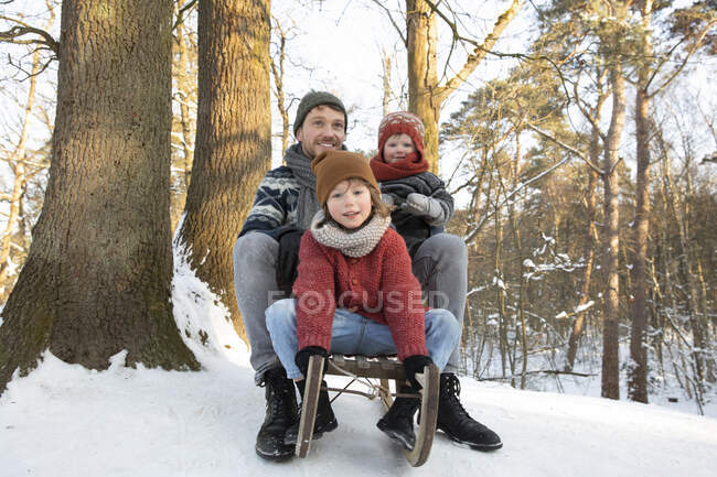 Vater sitzt im Winter mit Söhnen auf Schlitten neben Baumstamm — Stockfoto