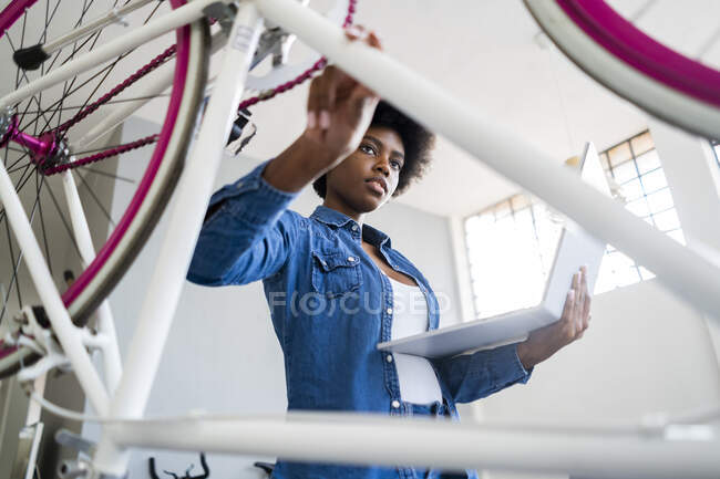 Junge Frau mit Laptop repariert Fahrrad zu Hause — Stockfoto