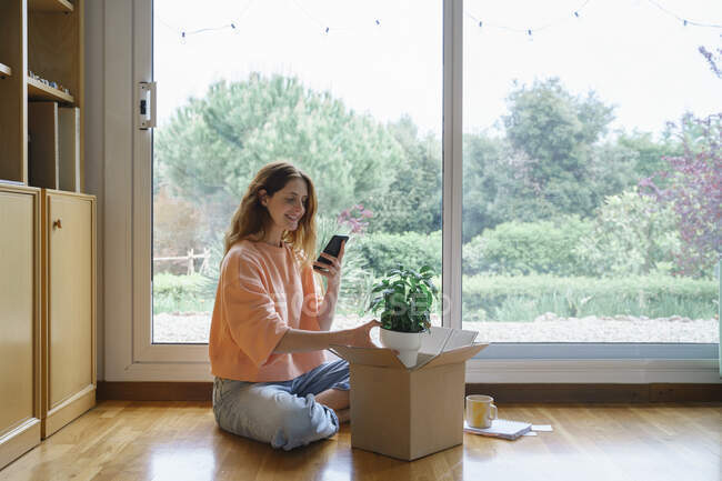 Mulher fotografar planta através de telefone inteligente enquanto sentado em casa — Fotografia de Stock
