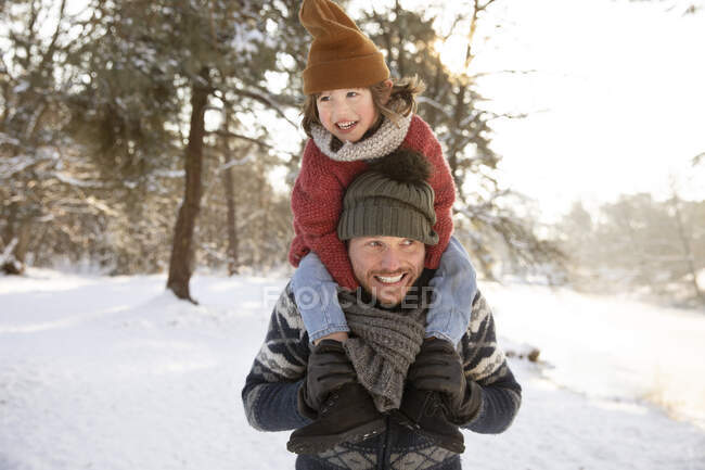 Père souriant regardant loin tout en portant son fils sur l'épaule pendant l'hiver — Photo de stock