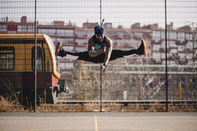 Homme africain utilisant un téléphone portable tout en sautant sur le terrain de sport — Photo de stock