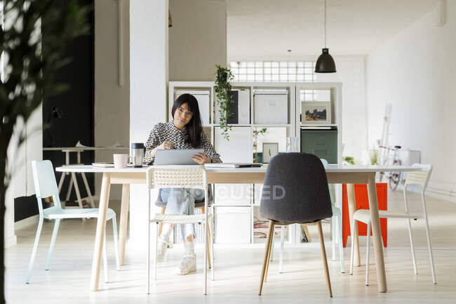 Женщина-предприниматель с графическим планшетом сидит на столе в офисе — стоковое фото