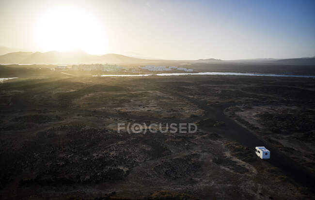 España, Islas Canarias, Vista aérea de autocaravanas conduciendo hacia el sol naciente a lo largo de la carretera de grava en la isla de Lanzarote - foto de stock