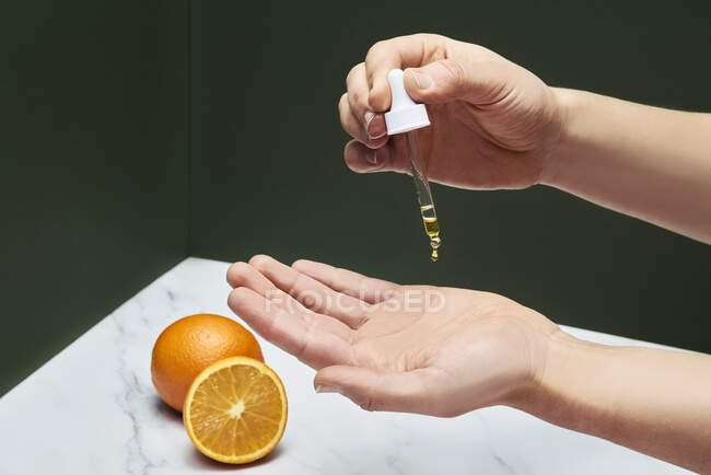 Woman taking drop of serum on hand through dropper over table — Stock Photo
