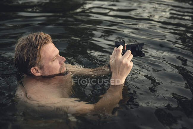 Uomo nuotare nel lago, scattare foto con la sua macchina fotografica — Foto stock