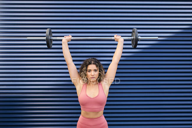 Mujer atleta levantando la barra delante de la pared acanalada azul - foto de stock