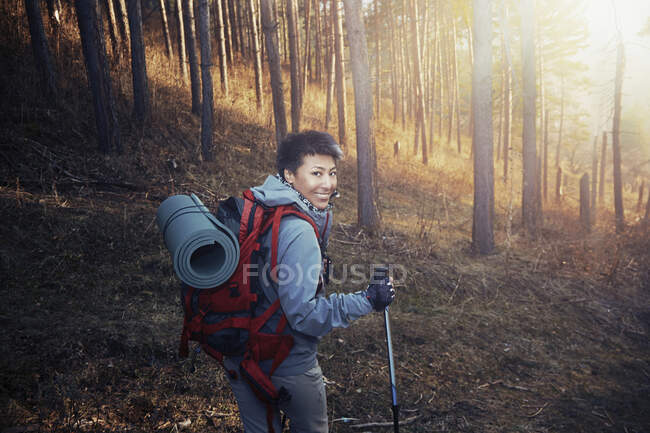 Smiling woman with backpack looking over shoulder while hiking in woodland — Stock Photo