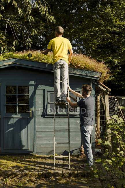 Padre in piedi sulla scala sostenuto dal figlio di fronte alla casa — Foto stock