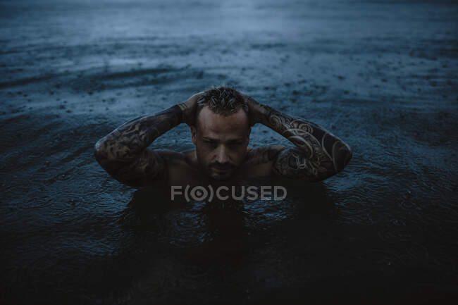 Hipster man with hands behind head in sea in rain — Stock Photo