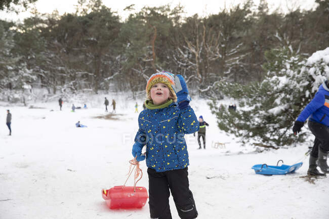 Garçon ludique avec toboggan debout sur la neige — Photo de stock