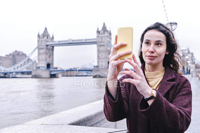 Mulher tirando selfie através do telefone celular enquanto Tower Bridge no fundo — Fotografia de Stock