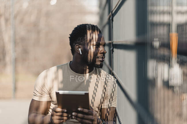 Молодой человек смотрит в сторону, держа в руках цифровой планшет в солнечный день — стоковое фото