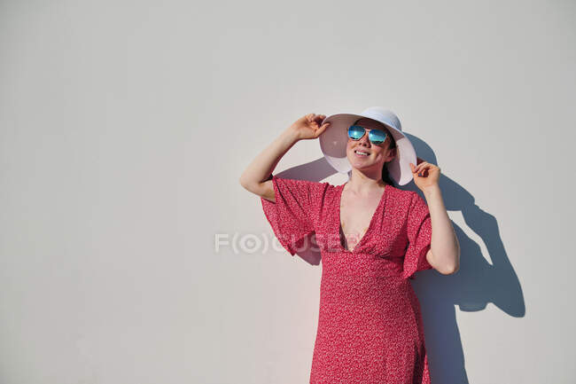 Donna che tiene il cappello da sole da parete bianca durante la giornata di sole — Foto stock