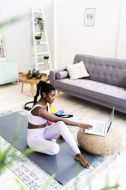 Jeune femme utilisant un ordinateur portable tout en étant assis sur le tapis d'exercice à la maison — Photo de stock