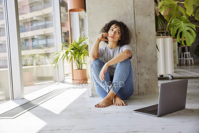 Junge Frau schaut weg, während sie zu Hause auf dem Boden sitzt — Stockfoto