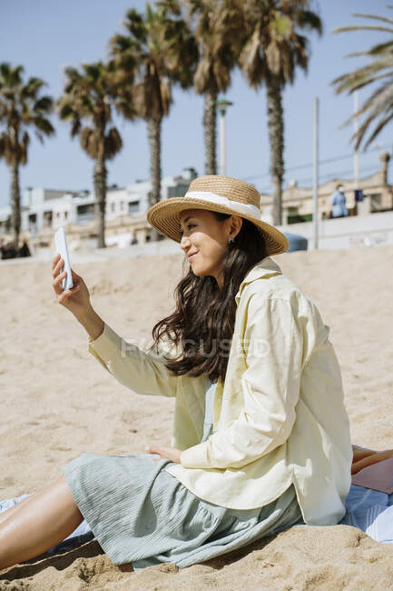 Женщина делает селфи, сидя на пляже — стоковое фото