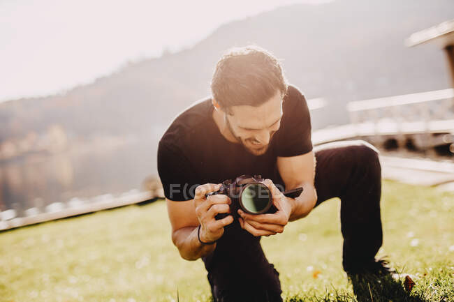 Jovem agachado enquanto usa a câmera no gramado — Fotografia de Stock