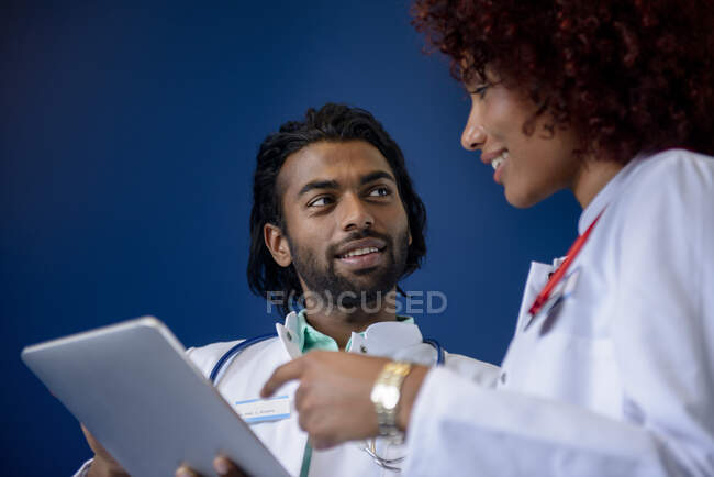 Médicos masculinos y femeninos discutiendo sobre tableta digital contra fondo azul - foto de stock