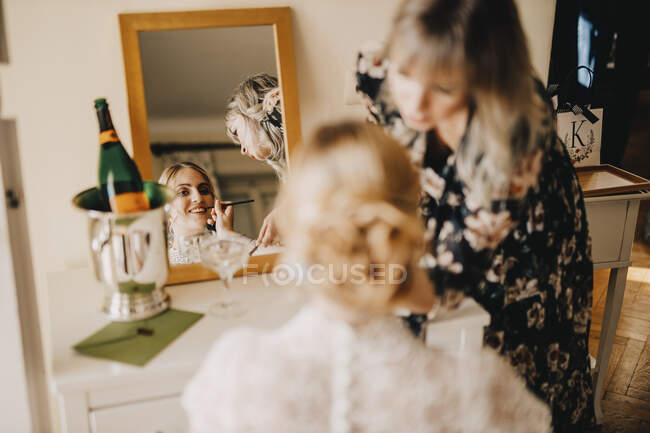 Novia mirando en el espejo mientras esteticista aplicar maquillaje durante la boda - foto de stock