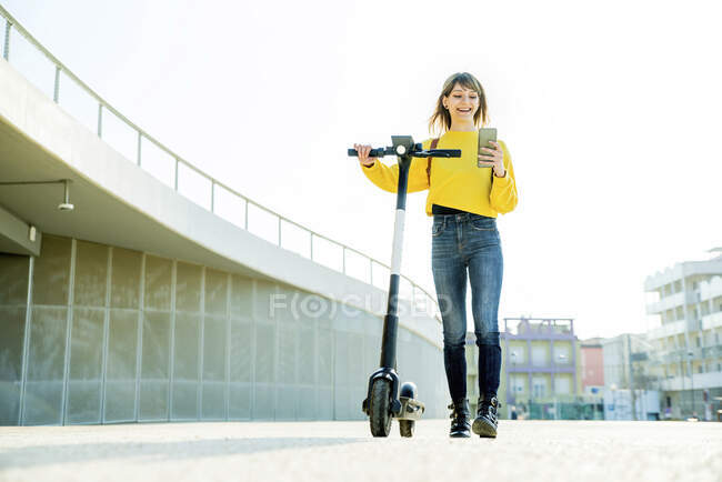 Женщина пользуется смартфоном во время прогулки на электросамокате — стоковое фото