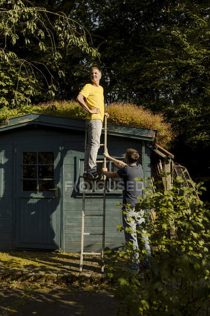 Thoughtful man standing on ladder supported by son in back yard — Stock Photo