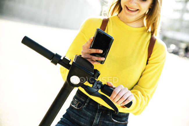 Jeune femme utilisant un téléphone intelligent pour déverrouiller scooter électrique push — Photo de stock