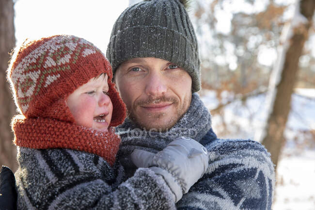 Отец в вязаной шляпе, держащий плачущего сына зимой — стоковое фото
