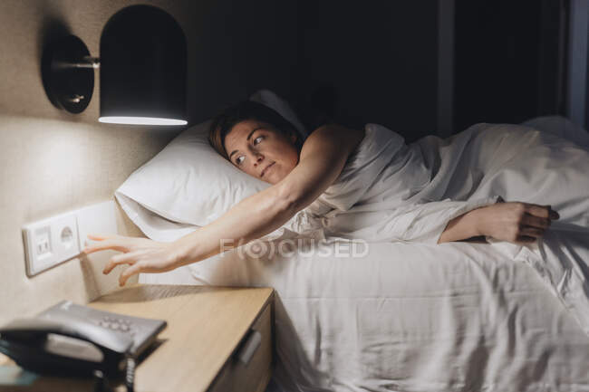 Mujer adulta media apagando la luz mientras está acostada en la cama - foto de stock
