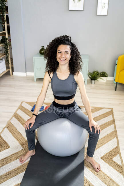 Femme heureuse assise sur le ballon de fitness dans le salon — Photo de stock