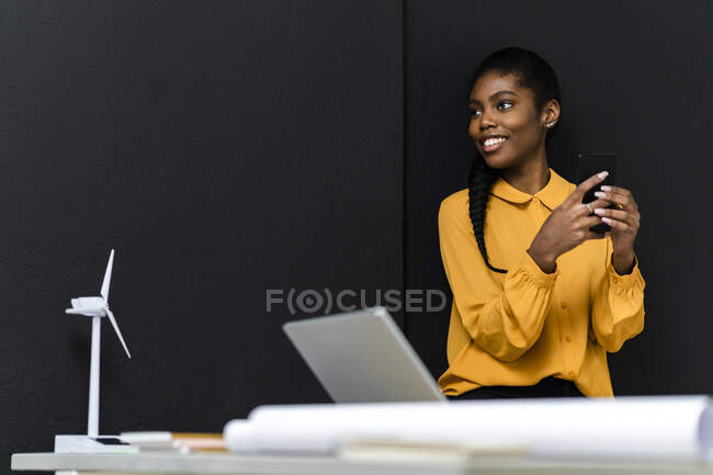 Smiling businesswoman holding mobile phone while looking away in studio — Stock Photo